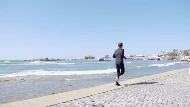 Νέος ελκυστικός ταιριάζει Καυκάσιος άνθρωπος σε μαύρο τρέχει σε μια αποβάθρα. Πίσω βολή αργή κίνηση — Αρχείο Βίντεο