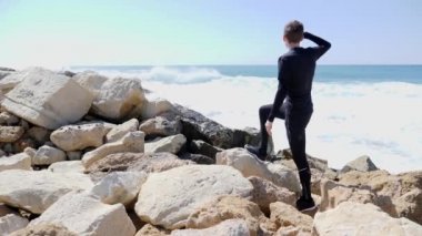 Genç adam el ile okyanusa bakarak vardı ve kayalıkların üzerinde duran ufukta parmak işaret. Su sıçramaları, kayalıklar.