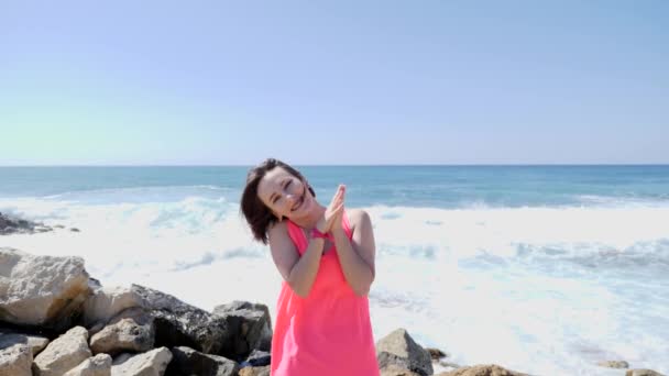 Giovane bella giostra felice battendo le mani e saltando su una spiaggia rocciosa mare con onde e spruzzi d'acqua. Giornata di sole ventosa. Rallentatore — Video Stock