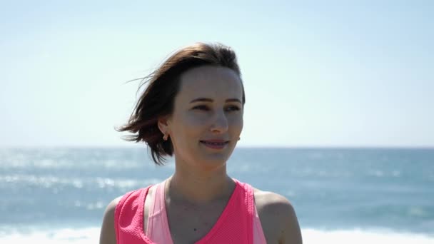 年轻美丽的适合高加索妇女肖像微笑着站在海滩上的相机。慢动作 — 图库视频影像