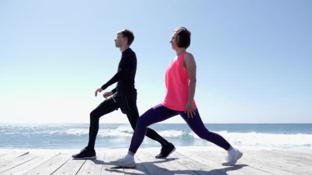 Young athletic man and woman stretching on the beach. Sea waves on the back ground. — Stock Video