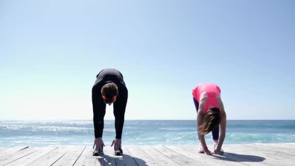 Joven hombre y mujer en forma haciendo ejercicios de estiramiento en un día soleado en la playa. Movimiento lento — Vídeo de stock