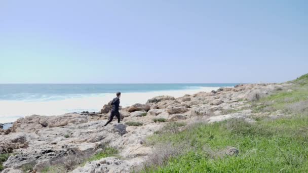 젊은 맞는 백인 남자 바다를 따라 바위 흔적에 실행. 백 샷 — 비디오