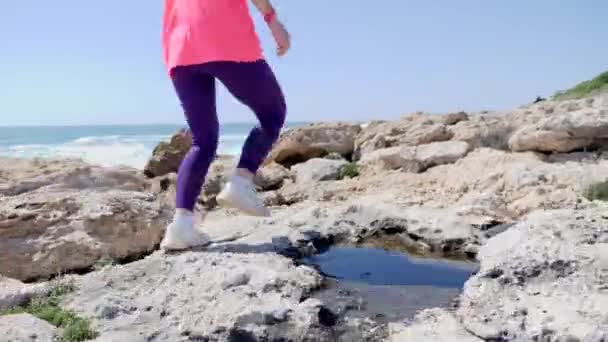 Mujer joven en forma corre el sendero rocoso a lo largo de la playa. El sendero corre sobre las rocas. Moción lenta . — Vídeo de stock