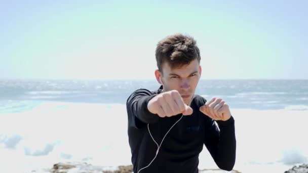 Der junge, motivierte Boxer schlägt in die Luft und blickt direkt in die Kamera. Boxtraining am Strand. Nahaufnahme. Zeitlupe — Stockvideo