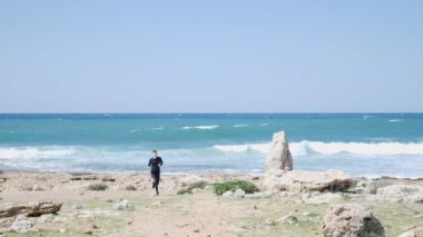 Genç uygun beyaz adam sahilde kameraya doğru çalışıyor. Backgound üzerinde güçlü dalgalar ile deniz. Yavaş hareket