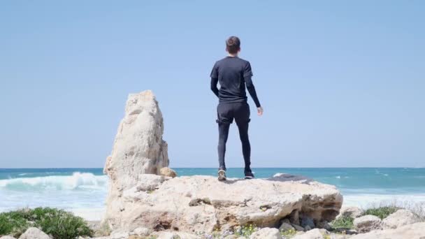 Young fit man running to the big rock and puts his fist in the air celebrating victory. Man standing on the rock with the hands up — Stock Video