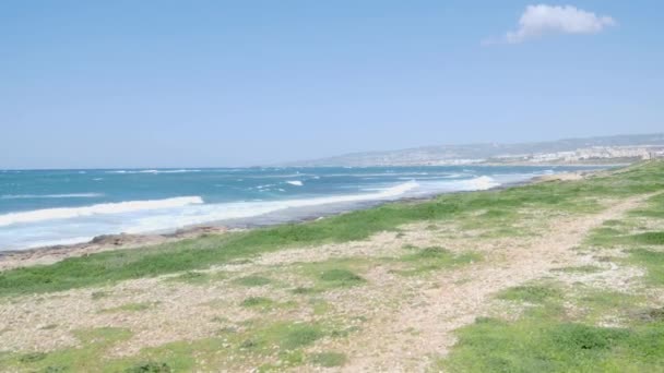 Giovane uomo caucasico magro che corre sulla spiaggia indossando abiti neri e occhiali da sole. Il mare ondulato è sullo sfondo. Rallentatore — Video Stock