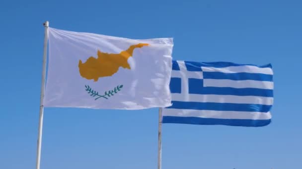 Kıbrıs ve Yunan bayrakları rüzgarda bir direğe çarpıyor. Mavi gökyüzü, Yunan ve Kıbrıs bayrağı. — Stok video