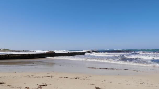 An einem sonnigen, windigen Tag schlagen starke Wellen gegen die Seebrücke und den Sandstrand. Zypern Strand stürmisches Wetter — Stockvideo