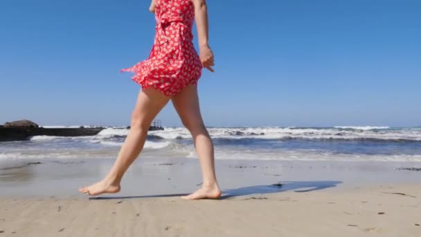 Jambes de jeune femme marchant sur la plage de sable avec de fortes vagues. Jeune femme portant une robe rouge marchant le long de la plage à Chypre seul. Mouvement lent — Video