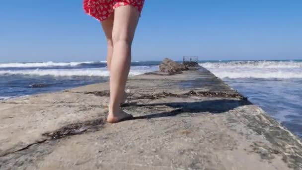 Piernas de mujer joven caminando sobre el muelle descalzo con fuertes olas golpeando contra el muelle . — Vídeos de Stock