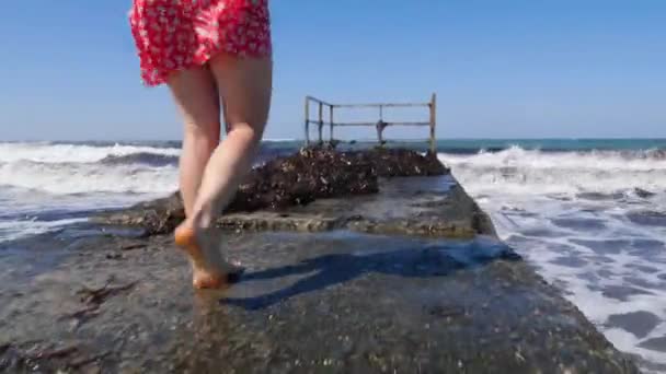 Jovem mulher feliz andando no cais em direção ao mar tempestuoso com ondas espalhando as mãos para além posando. Forte vento e ondas salpicando . — Vídeo de Stock