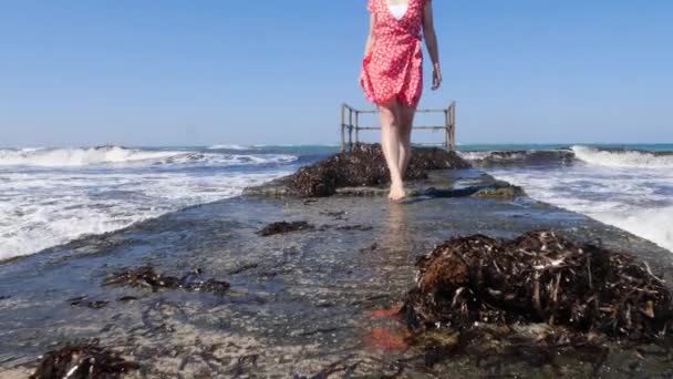 Joven hermosa mujer caminando sobre el muelle del mar descalzo con las olas salpicando contra el muelle. Las piernas se cierran. Movimiento lento — Vídeo de stock