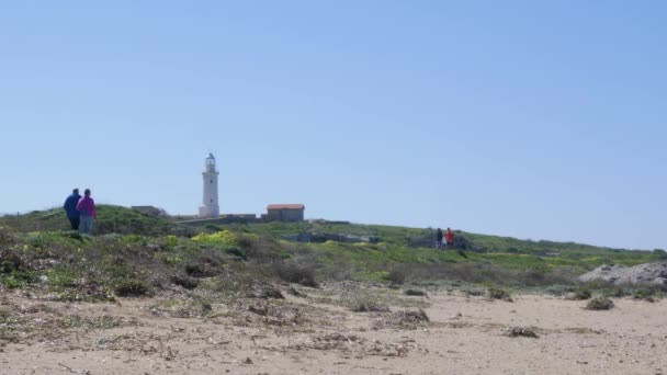 Piétons marchant sur la promenade maritime avec phare par une journée ensoleillée et venteuse à Chypre . — Video