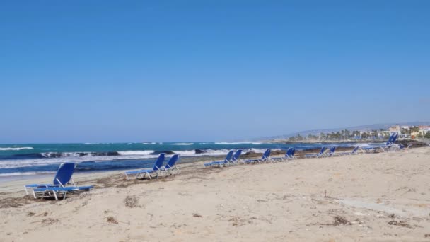 Tiro de la solitaria playa de arena con tumbona en el tormentoso día ventoso. Fuertes olas golpeando y salpicando contra la orilla del mar . — Vídeo de stock