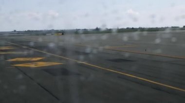 Uçak hareket ederken havaalanı pistinde yağmur damlaları ile uçak penceresinden görünümü