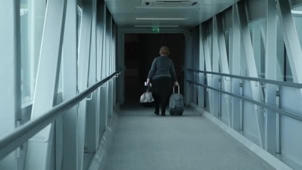 Back view of old woman with hand baggage boarding the plane walking through the gate bridge at the airport terminal. Travel concept — Stock Video