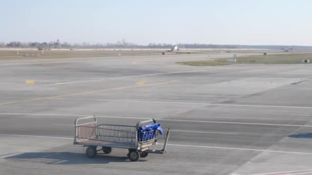 Carrello bagagli vuoti all'aeroporto. Trattore con carrelli bagagli emty che passano vicino all'aereo . — Video Stock