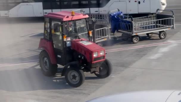 Rastreador com carrinhos de bagagem vazios passando pelo avião. Pessoal carro está se movendo perto do avião . — Vídeo de Stock