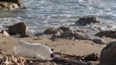Dalgalar sıçrayan kumlu plajda plastik şişe. Plastik çöp kirliliği kavramı. Yavaş Çekim