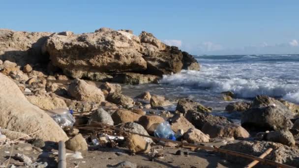 Kamienista plaża zanieczyszczona plastikowymi butelkami. Fale uderzając piaszczystej plaży z plastikowych butelek. — Wideo stockowe