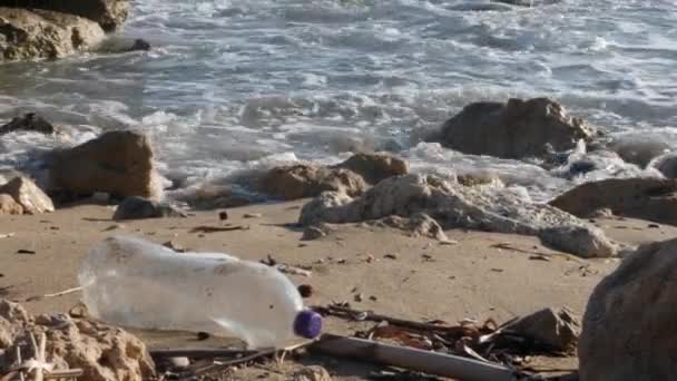 Botella de plástico en la playa de arena con olas salpicando. Concepto de contaminación de basura plástica . — Vídeos de Stock