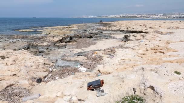ペットボトルやゴミで汚染されたロッキービーチ。漁師と船を背景にスローモーション — ストック動画