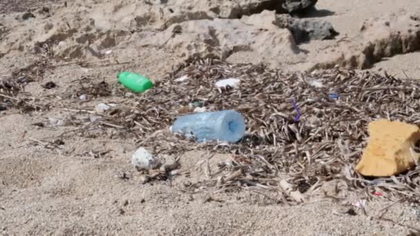岩の多い砂浜のペットボトルとストロー。プラスチック汚染の概念. — ストック動画