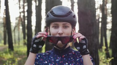 Young beautiful girl puts on cycling glasses wearing helmet and blue jersey. Road cycling concept. Slow motion
