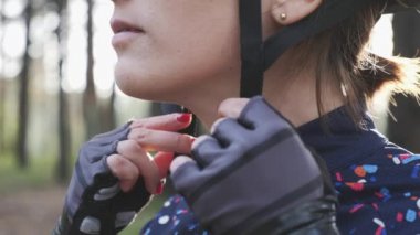 Young cyclist girl tightens harness on the helmet before the bicycle ride. Cycling concept. Slow motion