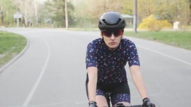 Parkta bisiklete binen odaklanmış kadın bisikletçi. Ön görüş. Siyah kask ve gözlük takmak.