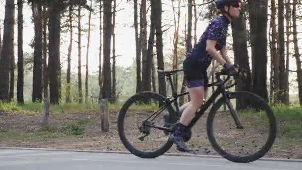 Gyönyörű kaukázusi kerékpáros lány indul pedaling ő közúti kerékpár a parkban visel kék trikó és fekete sisak. Országúti kerékpáros koncepció. — Stock videók