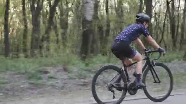 若いフィットの女性は公園で自転車に乗っている。木の間から太陽。後を追え. — ストック動画