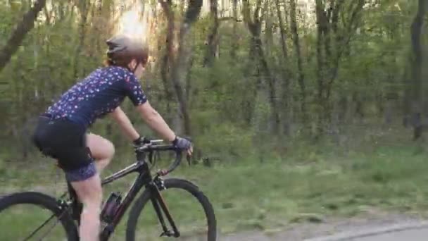 Ciclista fêmea montando uma bicicleta no pôr do sol no parque. Siga a vista lateral. Conceito de ciclismo e triatlo . — Vídeo de Stock