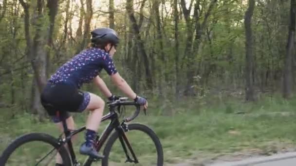 Mujer ciclista montando en bicicleta al atardecer en el parque. Siga la vista lateral. Concepto de ciclismo y triatlón. Movimiento lento — Vídeo de stock