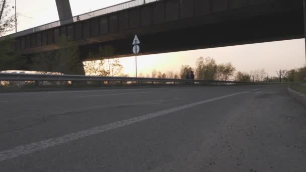 Mädchen reitet bei Sonnenuntergang mit Fahrrad aus dem Sattel in Richtung Brücke. — Stockvideo