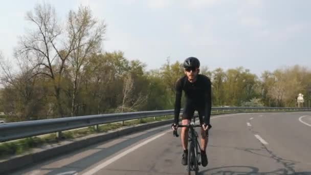 Εστιασμένη ποδηλάτης σε ένα οδικό ποδήλατο ιππασία προς την κάμερα στο ηλιοβασίλεμα. Ο μηχανόβιος φορούσε μαύρη φανέλα και σορτς. Ιδέα ποδηλασίας. — Αρχείο Βίντεο