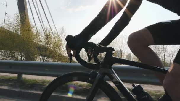 Ciclista masculino montando en bicicleta y cambiando de marcha. Sol brillando y puente sobre fondo. Acércate al siguiente disparo. Concepto de ciclismo. Movimiento lento — Vídeos de Stock