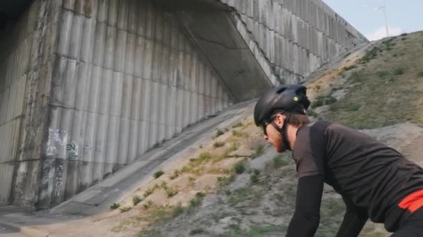 Joven ciclista masculino en forma montando bicicleta fuera de la silla de montar con traje negro, casco y gafas de sol. Concepto de ciclismo. Movimiento lento — Vídeos de Stock