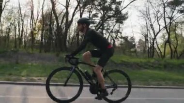 Bisikletçi parkta siyah bir profesyonel yol bisikleti sürme siyah mayo ve şort giyiyor. Yan takip atış. Bisiklet konsepti.