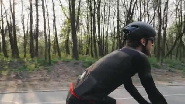 Бородатый велосипедист крутит педали на велосипеде в чёрном спортивном костюме, шлеме и очках. Велосипедная концепция. Медленное движение — стоковое видео