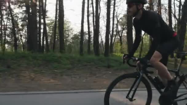 Fit confident cyclist on a bicycle out of the saddle in the park. Strong leg muscles spinning pedals. Cycling concept. Slow motion — Stock Video