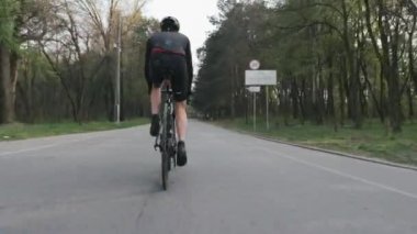 Bisikletle pedal çeviren bisikletçi bacak kası görünümüne yakın. Parktaki bisiklet sürücüsü siyah spor kıyafetler giyiyor.