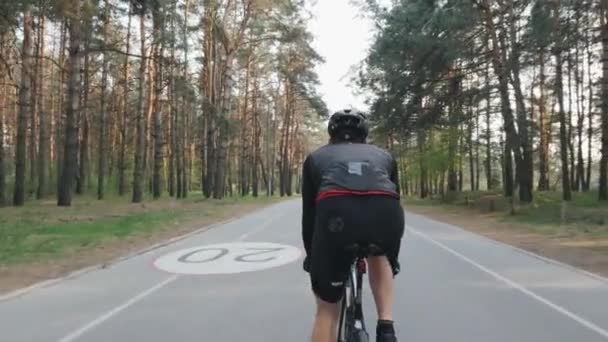 블랙 의상을 입고 자전거를 타고 핏 스포티 한 사이클리스트의 뒤를 따라. 강한 근육이 자전거 페달링 다리. 사이클링 컨셉. 슬로우 모션 — 비디오
