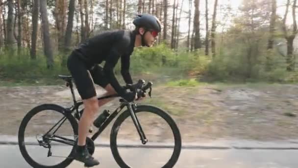 Andar de bicicleta lado seguir vista. Homem barbudo de roupa preta em bicicleta no parque. Fora da sela a pedalar. Movimento lento — Vídeo de Stock