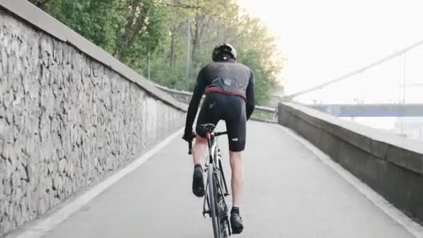 强壮的专业自行车手与瘦腿强壮的肌肉骑上坡出鞍。返回跟随拍摄。自行车训练. — 图库视频影像