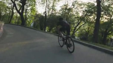 Parktaki yol bisikletine inen sıska atletik bisikletçi. Siyah bisiklete binen siyah kıyafet giyen bisikletçi. Bisiklet konsepti.