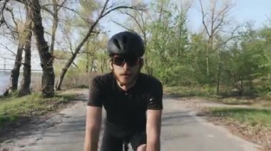 Parkta bisiklete binen rahat atletik fit bisikletçi. Ön takip atışı. Siyah kıyafet giyen sakallı bisikletçi bisiklete binmek kolay sürüş.