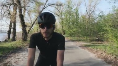 Parkta bisiklete binen rahat atletik fit bisikletçi. Ön takip atışı. Siyah kıyafet giyen sakallı bisikletçi bisiklete binmek kolay sürüş. Yavaş çekim